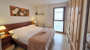 A hotel room with a bed, bedside lamps, a radiator, a window, and a wooden wardrobe. - Apartamentos Pilartxo Jaca 3000 (Jaca)