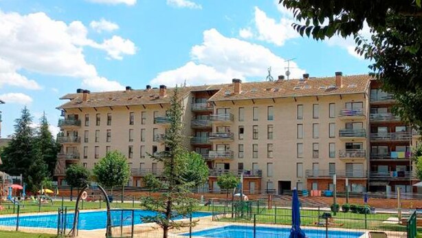 A residential building with multiple balconies, a swimming pool, and a grassy area with lounge chairs. - Apartamentos Pilartxo Jaca 3000 (Jaca)