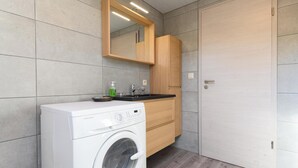 A compact bathroom with a washing machine, a sink, and a mirror. - Gite Le Clocher. Complete apartment overlooking the countryside. (Nassogne)