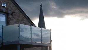 A house with a brick exterior, a balcony with a glass enclosure, and a weather vane on the roof. - Gite Le Clocher. Complete apartment overlooking the countryside. (Nassogne)