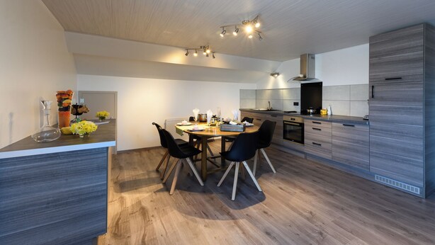 A modern kitchen with a dining area, wooden flooring, and built-in appliances. - Gite Le Clocher. Complete apartment overlooking the countryside. (Nassogne)