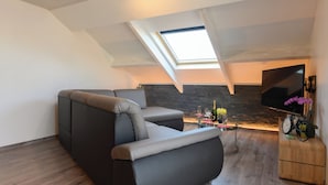 A modern loft apartment with a skylight, a sofa, a small table with drinks, and a TV. - Gite Le Clocher. Complete apartment overlooking the countryside. (Nassogne)