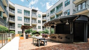 A courtyard with a brick patio, outdoor seating, and a covered barbecue area. - Luxury Apt Steps from Shopping & Dining, Free Parking, Resort Style Pool, Gym (San Antonio)