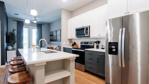 A modern kitchen with a central island, stainless steel appliances, and wooden stools. - Luxury Apt Steps from Shopping & Dining, Free Parking, Resort Style Pool, Gym (San Antonio)