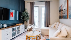 A modern living room with a flat-screen TV, a sofa, a coffee table, and a potted plant. - Luxury Apt Steps from Shopping & Dining, Free Parking, Resort Style Pool, Gym (San Antonio)