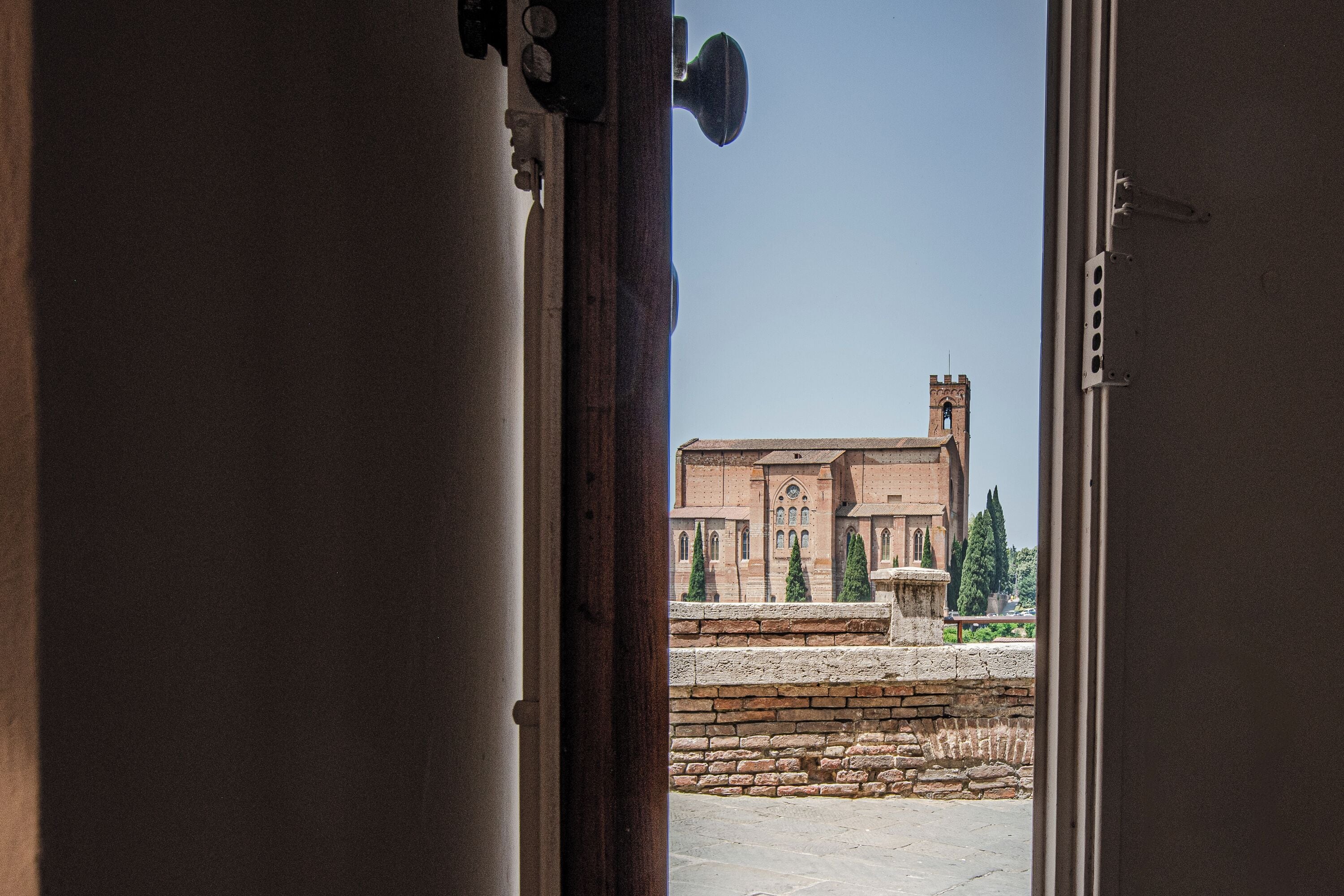 Une vue à travers l’encadrement d’une porte d’un bâtiment historique, avec un mur en pierre et une fontaine.