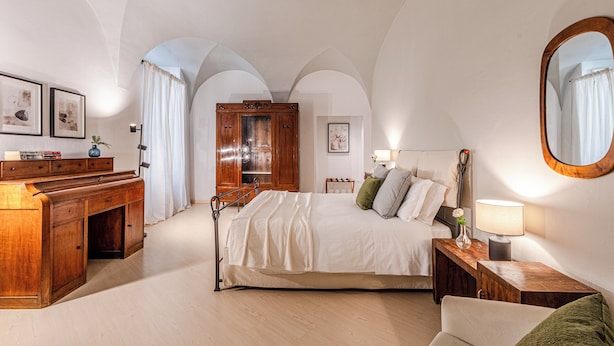 Une chambre à coucher comprenant un lit, un bureau en bois, une commode et une table de chevet avec une lampe.