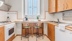 Une cuisine avec des meubles en bois, un four encastré, une fenêtre ornée de barreaux en fer décoratifs et deux tabourets de bar.