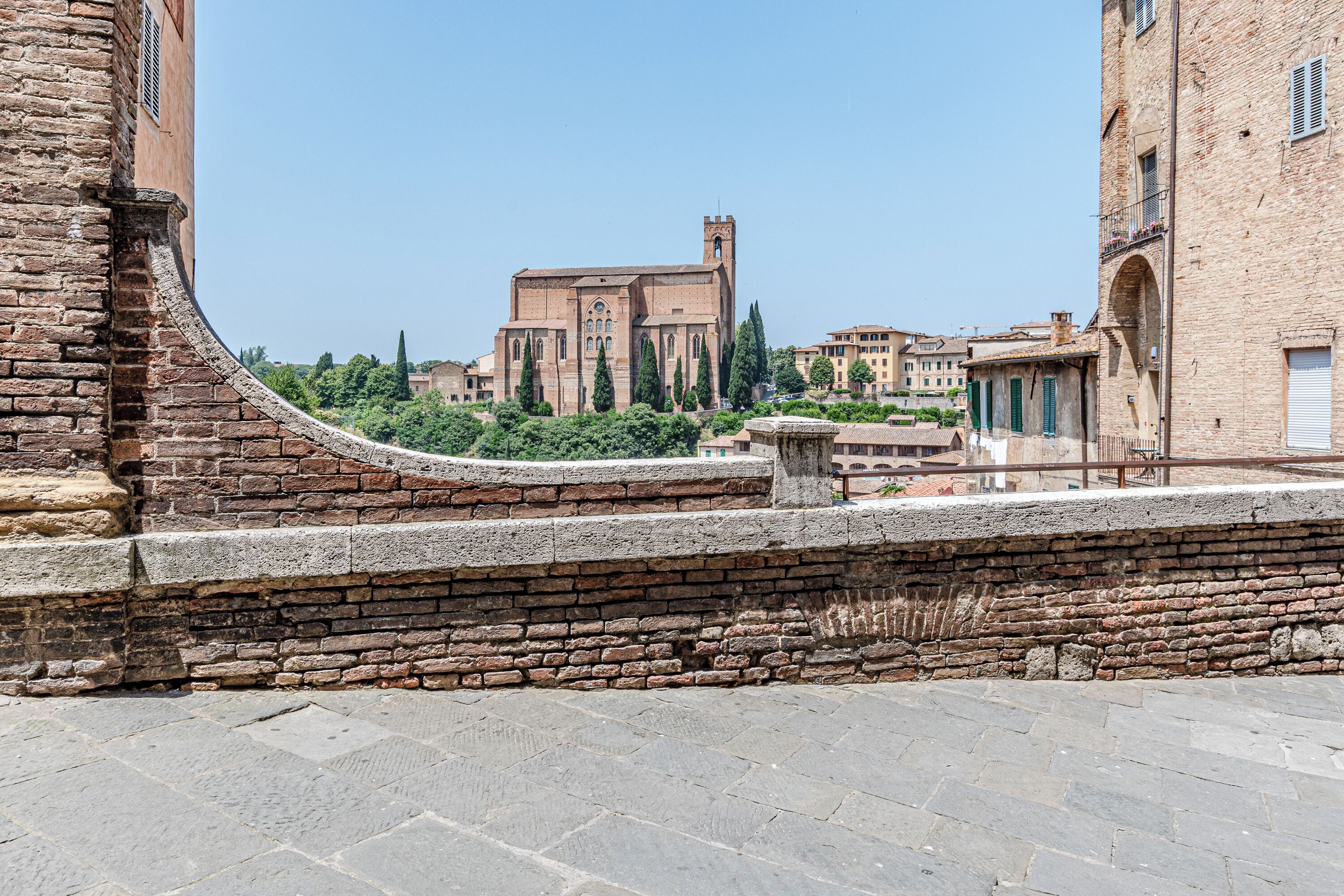 Un edificio storico in pietra con una torre imponente, circondato da altri edifici e vegetazione.