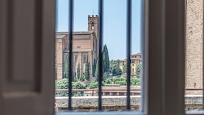 Une vue d’un bâtiment historique, dont la tour imposante est particulièrement visible, à travers une fenêtre ornée de barreaux verticaux.