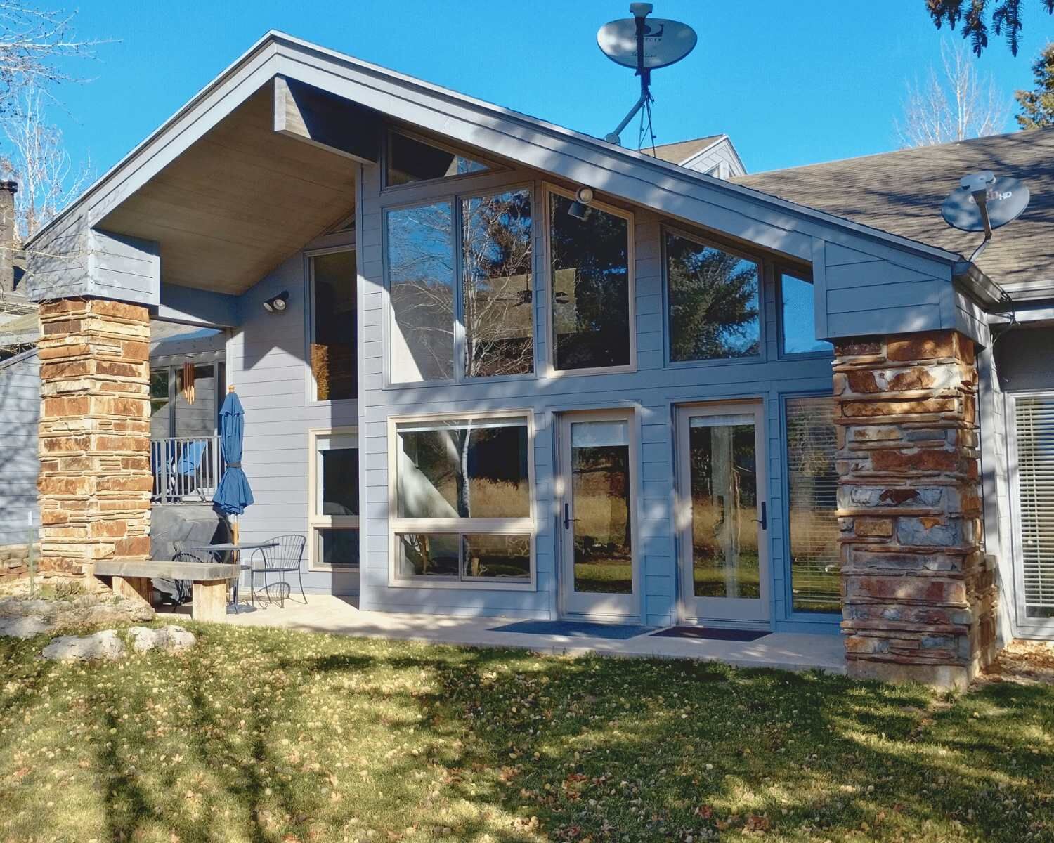 A modern two-story house with a stone foundation, large windows, and a satellite dish.