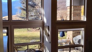 Ampia stanza con grandi finestre che si affacciano su un prato e montagne. È presente una zona relax con tavolo e sedie.