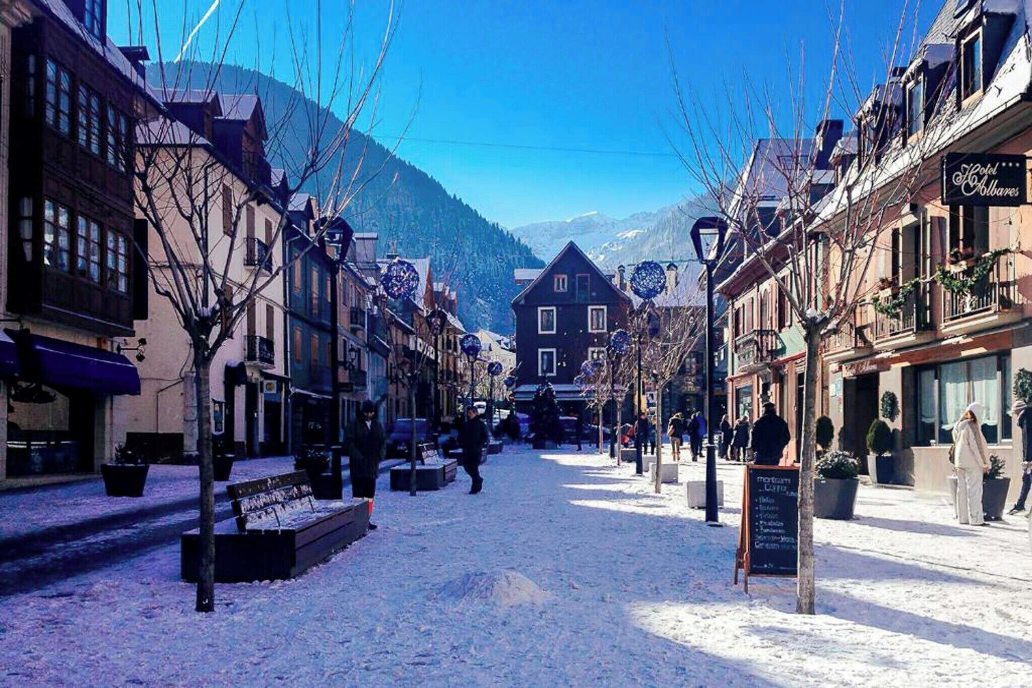 A snow-covered street with buildings, benches, and a signboard.