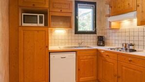 A kitchen with wooden cabinets, a microwave, a dishwasher, a window, and a stove. - À proximité des pistes ! Supebe studio avec balcon (Les Deux Alpes)