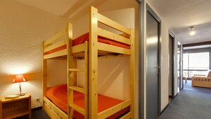 A bunk bed room with a wooden frame, orange bedding, a nightstand with a lamp, and a view of a balcony through a door. - À proximité des pistes ! Supebe studio avec balcon (Les Deux Alpes)