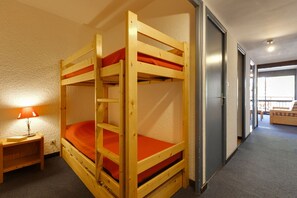 A bunk bed room with a wooden frame, orange bedding, a nightstand with a lamp, and a view of a balcony through a door. - À proximité des pistes ! Supebe studio avec balcon (Les Deux Alpes)