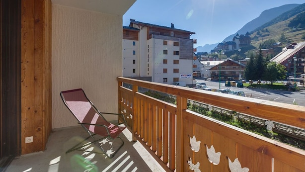 A balcony with a wooden railing and a folding chair, overlooking a town with buildings and mountains in the background. - À proximité des pistes ! Supebe studio avec balcon (Les Deux Alpes)
