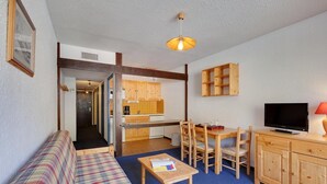 A cozy living room with a plaid sofa, a wooden dining table with chairs, a TV, and a kitchen area with wooden cabinets and a countertop. - À proximité des pistes ! Supebe studio avec balcon (Les Deux Alpes)