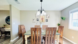 Un coin repas avec une table et des chaises en bois, un lustre et des œuvres d’art encadrées accrochées au mur.