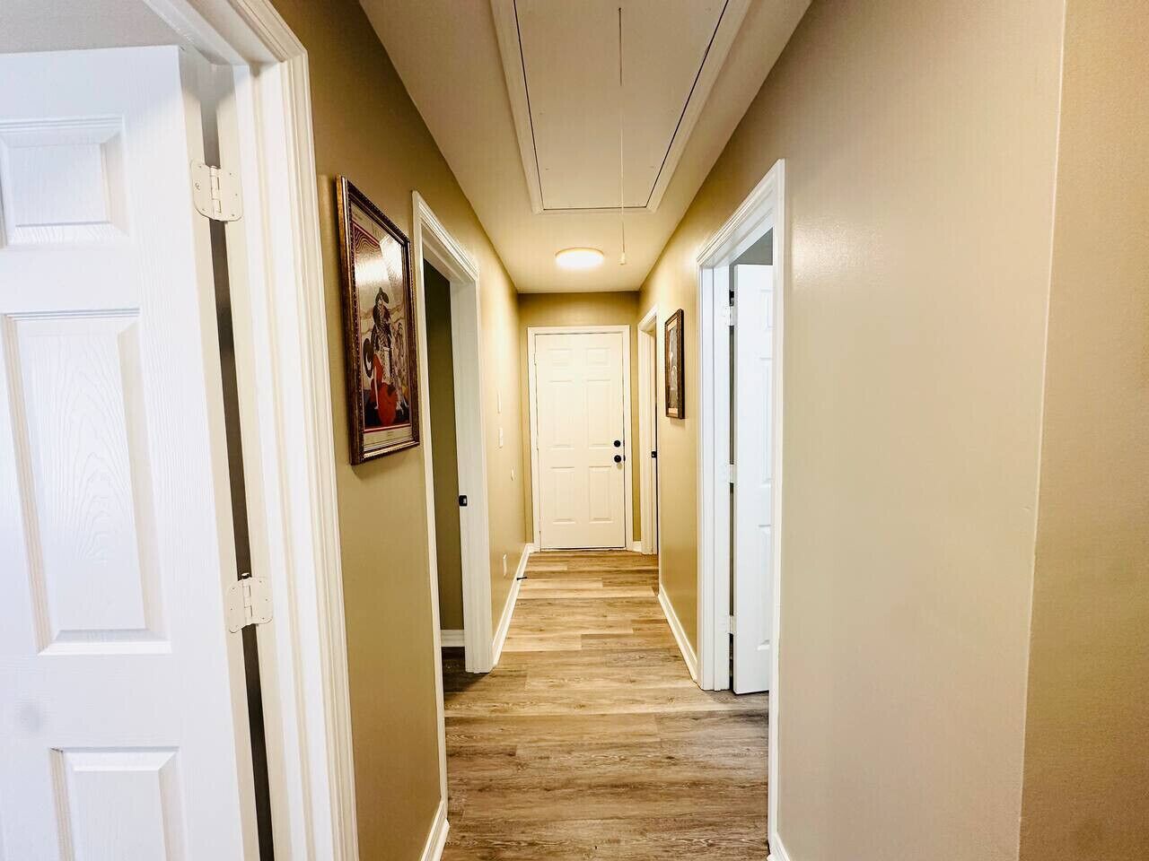 A hallway with wooden flooring, white doors, and framed pictures on the walls.