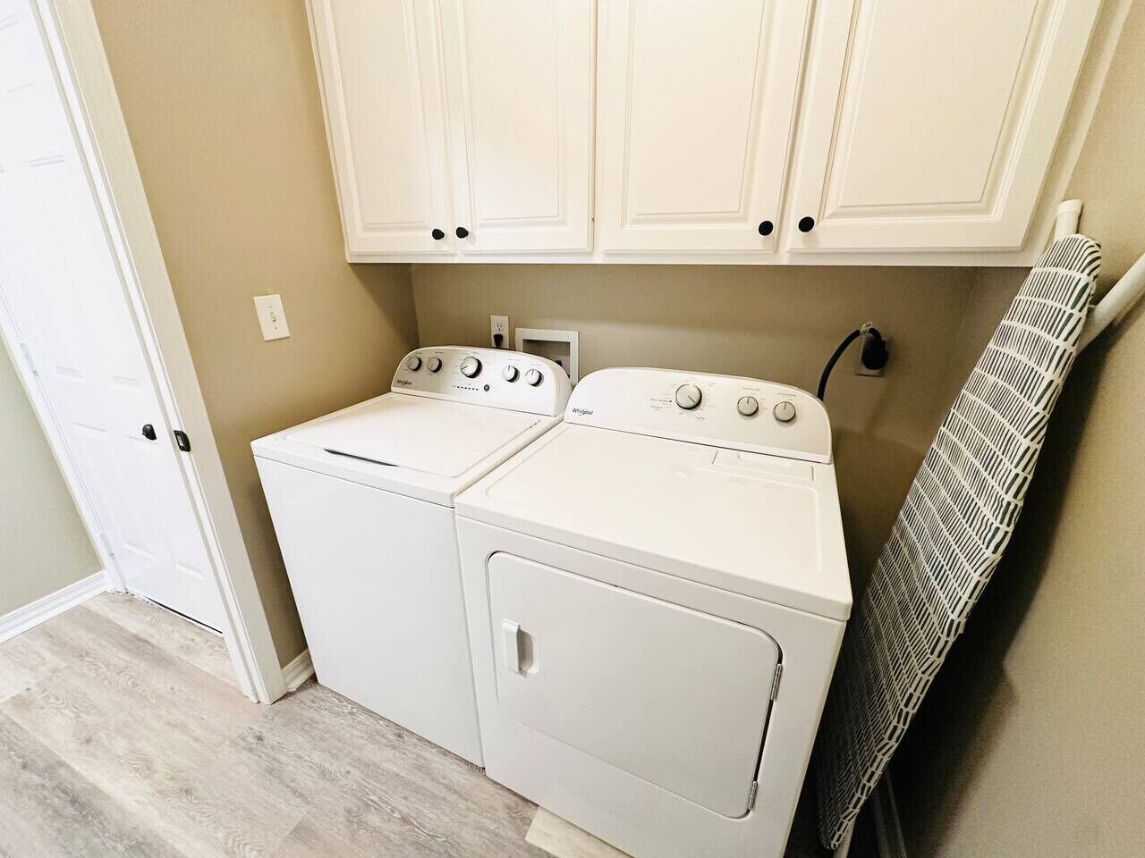 Een wasserij met twee witte wasmachines en een droger, muren in beige tint en een houten vloer.