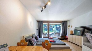 A cozy room with a bed, a TV, a dining table, and a view of a ski resort.