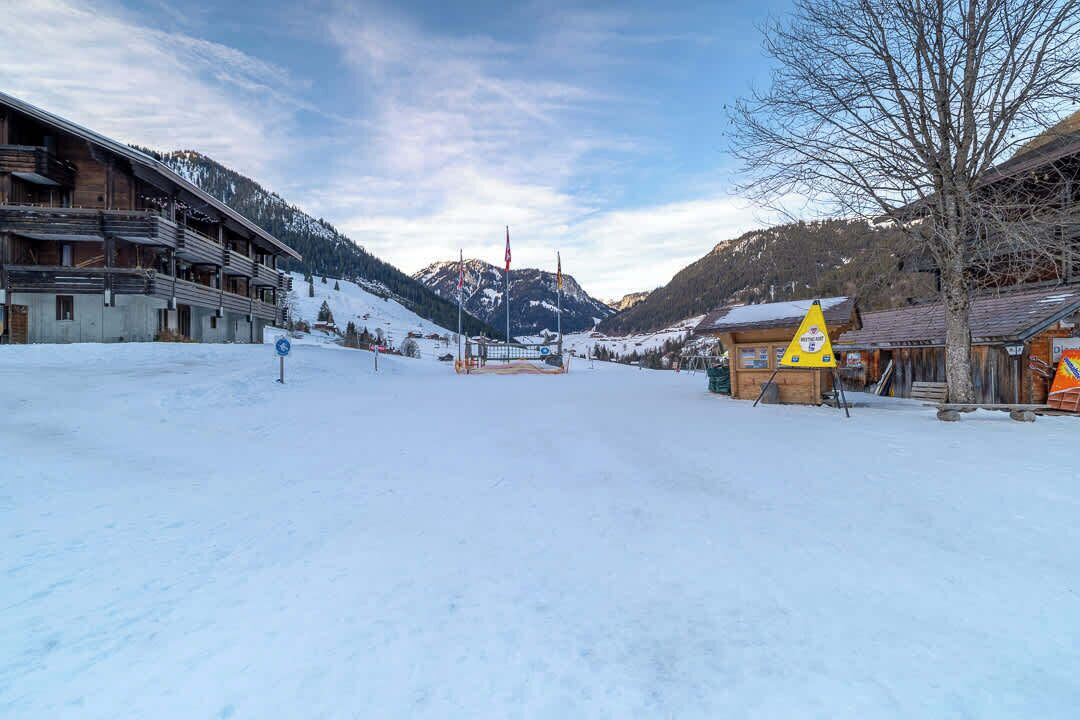 Ein verschneites Dorf mit Holzhäusern, einer Seilbahn und einem Berg im Hintergrund.