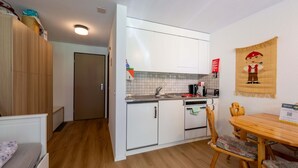 A compact kitchen with white cabinets, a wooden dining table, and a small seating area.