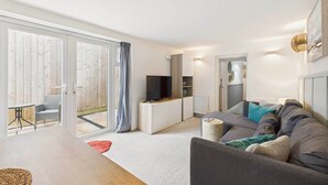 A modern living room with a grey sofa, a flat-screen TV, and a dining area with a wooden table. - Host Stay Surf Jewel (Saltburn-by-the-Sea)
