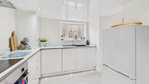 A modern kitchen with white cabinetry, a built-in stove, a sink, and a refrigerator. - Host Stay Surf Jewel (Saltburn-by-the-Sea)