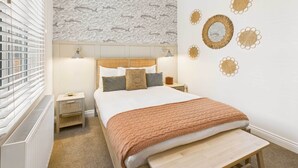 A neatly arranged bedroom with a bed, bedside tables, and a wall with decorative elements. - Host Stay Surf Jewel (Saltburn-by-the-Sea)