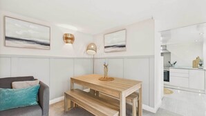 A modern living room with a grey sofa, a wooden dining table with benches, and two wall-mounted lamps. - Host Stay Surf Jewel (Saltburn-by-the-Sea)
