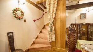 A staircase with a floral curtain, a wooden chair, and a table with a green tablecloth. - Host Stay The Spirit (Whitby)