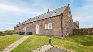 A stone house with a sloped roof, a front door, and a small patio area with outdoor furniture. - Host Stay Dolphin Dream (Berwick-upon-Tweed)
