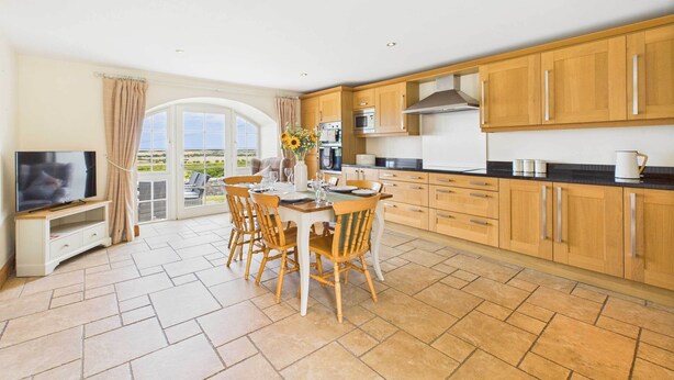 A spacious kitchen with wooden cabinets, a dining table with chairs, and a TV on a stand. - Host Stay Dolphin Dream (Berwick-upon-Tweed)