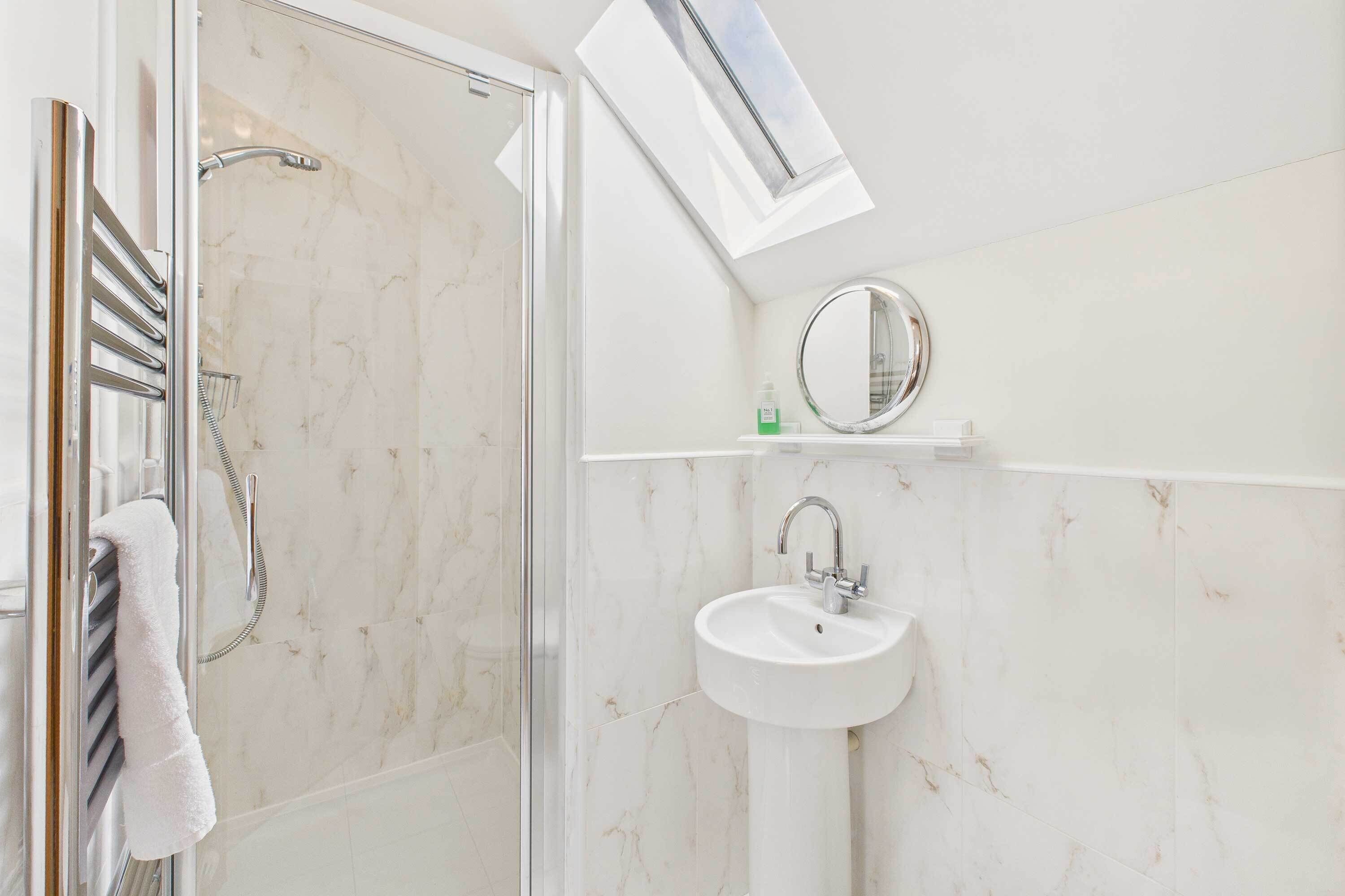 Een moderne badkamer met een glazen douchecabine, een witte wastafel en een spiegel op een witte plank.