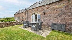 A stone building with a patio area featuring wicker furniture and a stone wall. - Host Stay Dolphin Dream (Berwick-upon-Tweed)