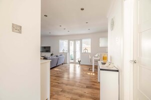 A bright, open-plan living area with a wooden floor, a sofa, and a dining table with a glass.