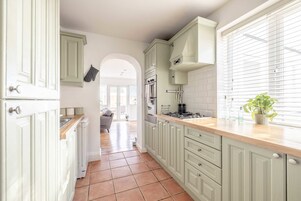 A kitchen with light green cabinets, a wooden countertop, and a window with blinds.