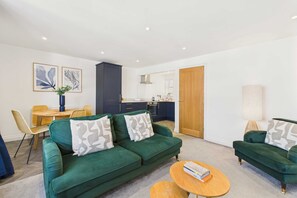 A modern living room with a green sofa, a wooden coffee table, and a dining area with a wicker table and chairs. - Host Stay Cringle Cottage (Middlesbrough)
