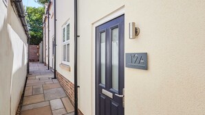 Un estrecho pasillo empedrado que conduce a una puerta azul oscuro con un letrero que dice "19A" y "Cringle Cottage".