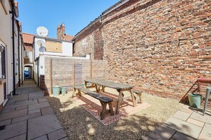 A courtyard with a wooden picnic table and benches, surrounded by a brick wall and a tiled pathway. - Host Stay Cringle Cottage (Middlesbrough)