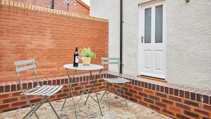 Un patio con una mesa, dos sillas, una botella de vino y una planta en maceta.