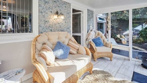 A sunlit room with two wicker sofas, a marble table, and a view of a garden through large windows. - Host Stay The Cheeky Squirrel (Wallasey)
