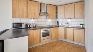 A modern kitchen with wooden cabinets, a stainless steel range hood, a microwave, a kettle, and a sink. - Host Stay 608 Hatton Garden (Liverpool)