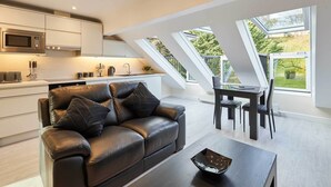 Een moderne keuken met een ingebouwde magnetron, een zithoek met tafel en stoelen, en een leren bank met kussens.