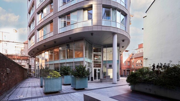 Un edificio moderno con facciata curva, ampie finestre e ingresso coperto. Davanti, vasi con piante verdi.