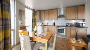 Una cucina moderna con mobili in legno, un tavolo da pranzo con sedie e vista sulla città attraverso ampie finestre.