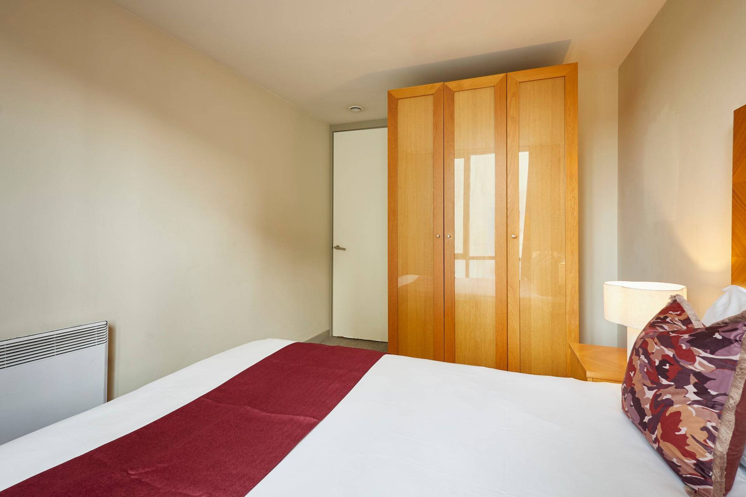 A hotel room with a bed, a wardrobe, a bedside table, and a lamp.