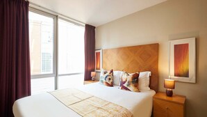 Una camera d'albergo con un letto grande, una testiera in legno, due comodini con lampade e una finestra con tende.